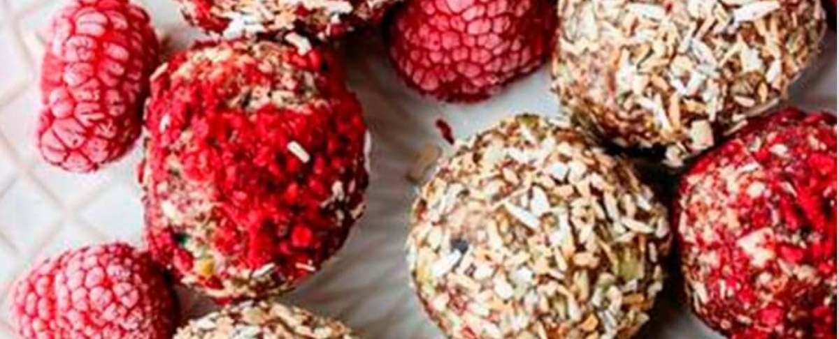 Close-up of CBD-infused raspberry energy bites showing shredded coconut and crushed raspberry coatings on a white patterned plate