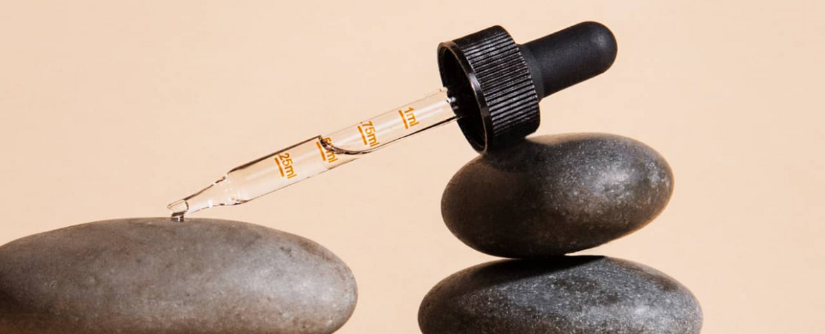 A dropper bottle of CBD and CBG oil tincture resting on stacked stones