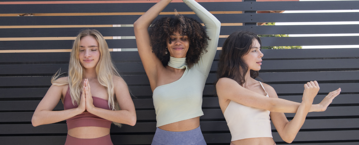 Three women practicing meditation in stylish activewear against a slatted backdrop.