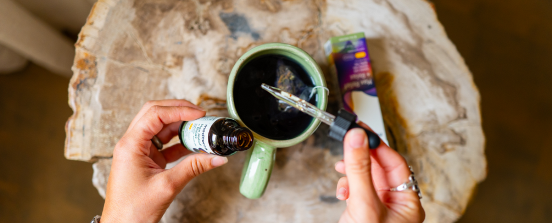 Person adding CBD oil to a cup of coffee on a wooden table.