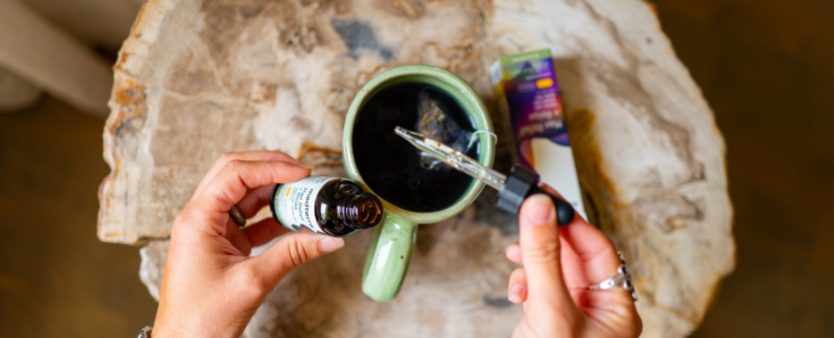 Person adding CBD oil to a cup of coffee on a wooden table.