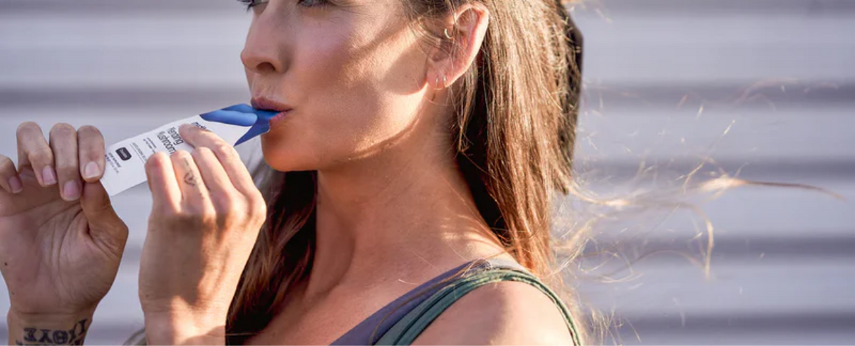 A woman using a product for workout recovery, holding a tube to her mouth.