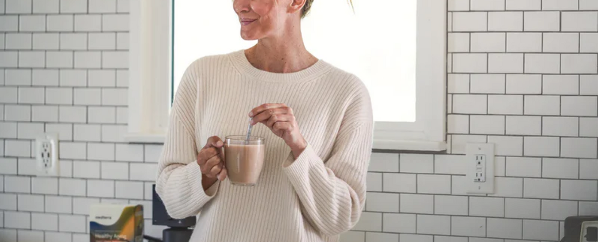 A woman in a cozy sweater holding a mug in a kitchen setting.