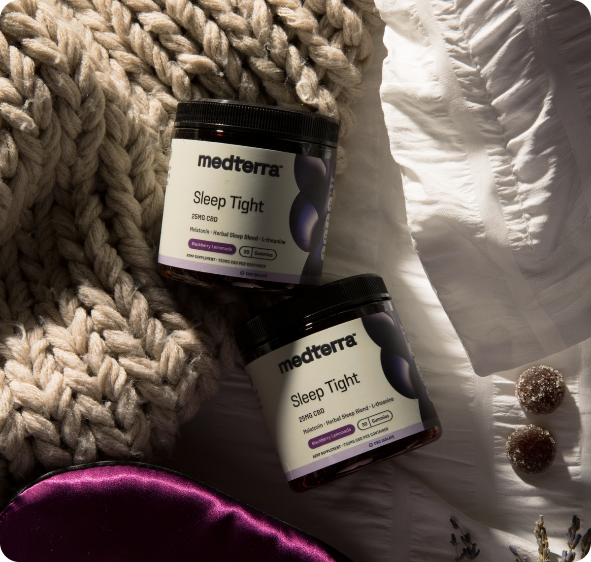Two Medterra Sleep Tight 25MG CBD gummy jars on a knit blanket and sheet, two sugar-coated gummies at right.
