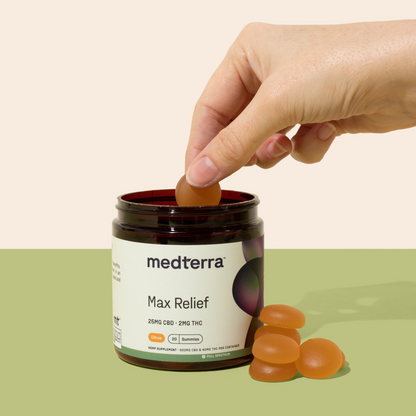 A hand reaches into a jar of Medterra Max Relief Full Spectrum CBD Gummies, holding one gummy above the open jar. The label on the jar indicates 25mg of CBD and 2mg of THC per gummy for achieving the entourage effect. Several gummies are scattered beside the jar, all set against a pastel background.