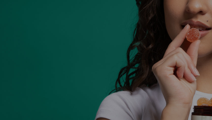 A person with long dark hair is holding a red gummy candy near their mouth, against a green background. Their eyes are looking slightly to the side.