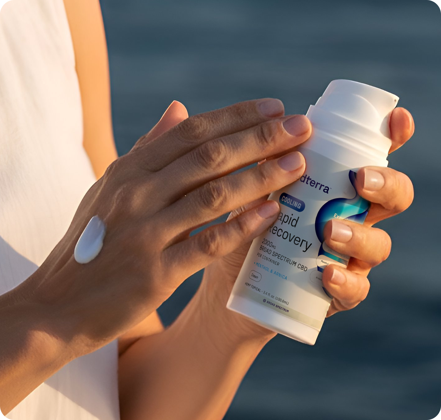 A person applies Medterra Rapid Recovery Cooling 2000mg CBD Cream to the back of their hand against a blurred blue background, seeking muscle relief.
