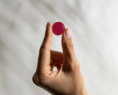 A hand with medium skin tone holds a small, round, deep pink Deep Sleep Gummy from Medterra CBD's Top 10 collection between the thumb and index finger against a light, blurry background. The fingernails are short and well-groomed.