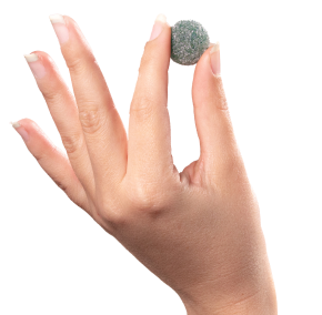 A close-up image showcases a hand with neatly manicured nails holding a small, round, greenish-gray object between its thumb and index finger. The background is plain white, highlighting the quality pure ingredients sourced from the USA, reminiscent of Medterra's commitment to excellence.