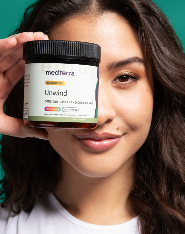 A person with long brown hair is smiling and holding a jar of Medterra Unwind gummies close to their face. The jar label indicates 50mg CBD, 5mg THC, 100mg L-Theanine, and a multi-flavor option. Made with pure ingredients grown in the USA, the background is a solid teal color.