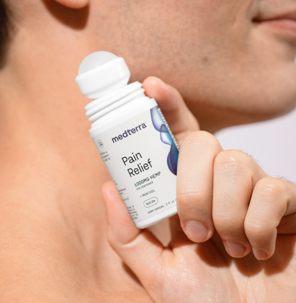 Person applying Medterra Pain Relief roll-on to their neck. The product label indicates it contains 1000mg of hemp and menthol.